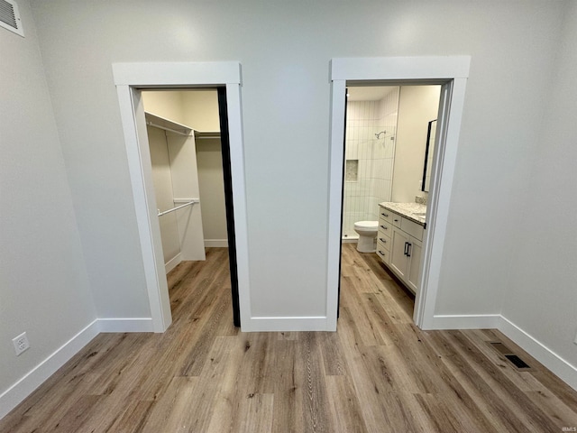 unfurnished bedroom with light hardwood / wood-style flooring, a spacious closet, ensuite bathroom, and a closet