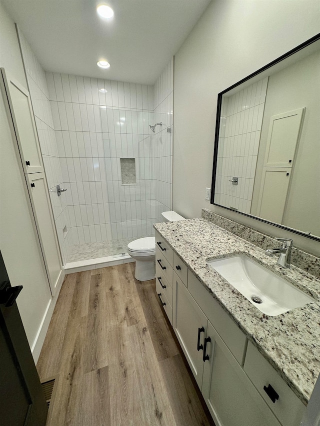 bathroom with wood-type flooring, toilet, a tile shower, and vanity