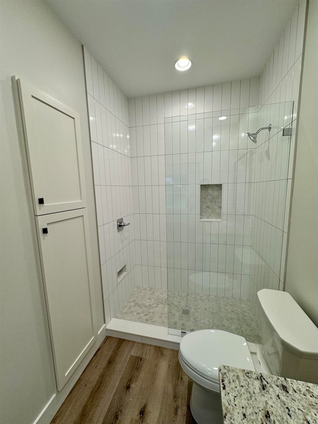 bathroom featuring toilet, a tile shower, and hardwood / wood-style floors