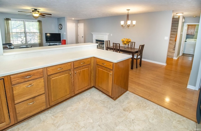 kitchen featuring washer / dryer, decorative light fixtures, kitchen peninsula, ceiling fan with notable chandelier, and light hardwood / wood-style floors