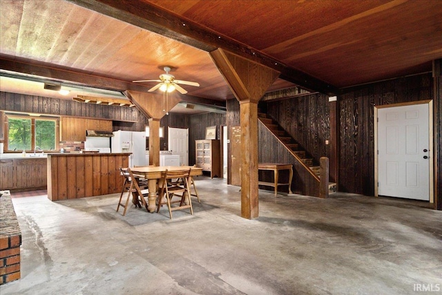 dining room featuring concrete flooring, wooden walls, and ceiling fan