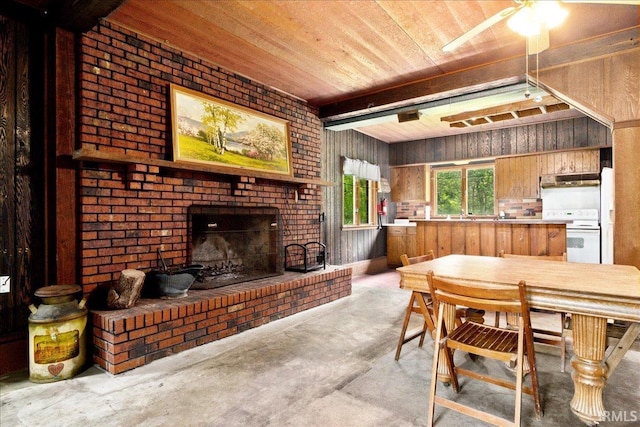 dining area featuring ceiling fan, wooden ceiling, brick wall, concrete floors, and a brick fireplace