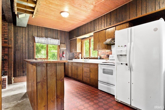 kitchen with dark tile patterned floors, white appliances, wood walls, wooden ceiling, and sink