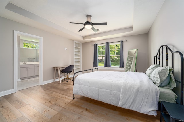 bedroom featuring sink, ensuite bath, light wood-type flooring, a raised ceiling, and ceiling fan