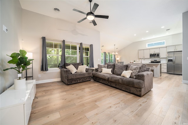 living room featuring vaulted ceiling, ceiling fan with notable chandelier, and light hardwood / wood-style floors