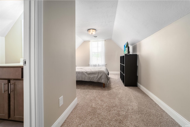 bedroom with vaulted ceiling, light carpet, and a textured ceiling