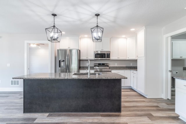 kitchen featuring a center island with sink, stainless steel appliances, sink, and dark stone counters