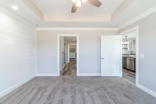 unfurnished bedroom with ceiling fan with notable chandelier, a tray ceiling, and crown molding