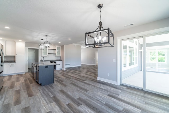 kitchen featuring dark hardwood / wood-style floors, decorative light fixtures, white cabinetry, an island with sink, and a chandelier