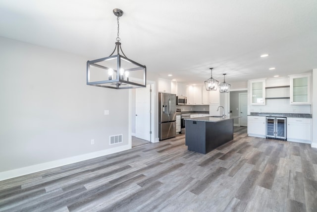 kitchen featuring an island with sink, decorative light fixtures, appliances with stainless steel finishes, and white cabinetry