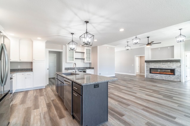 kitchen with ceiling fan with notable chandelier, a fireplace, a kitchen island with sink, sink, and white cabinets