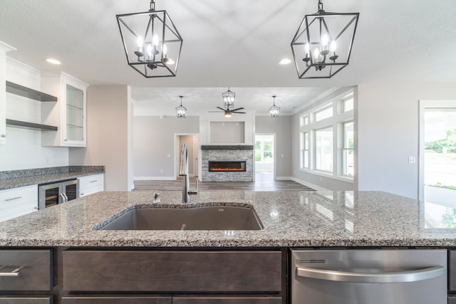 kitchen featuring a stone fireplace, pendant lighting, dishwasher, white cabinetry, and sink