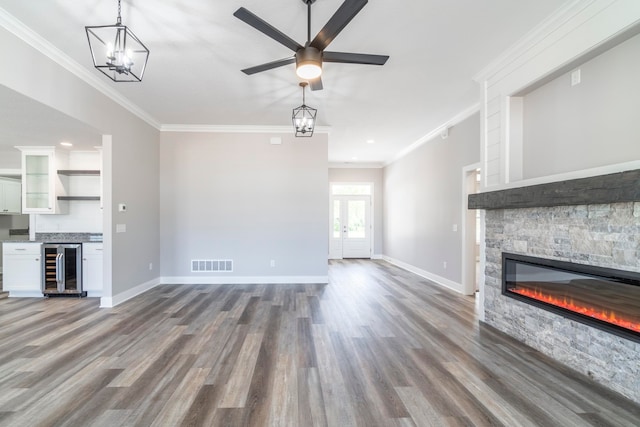 unfurnished living room featuring wine cooler, ceiling fan with notable chandelier, a fireplace, crown molding, and hardwood / wood-style flooring