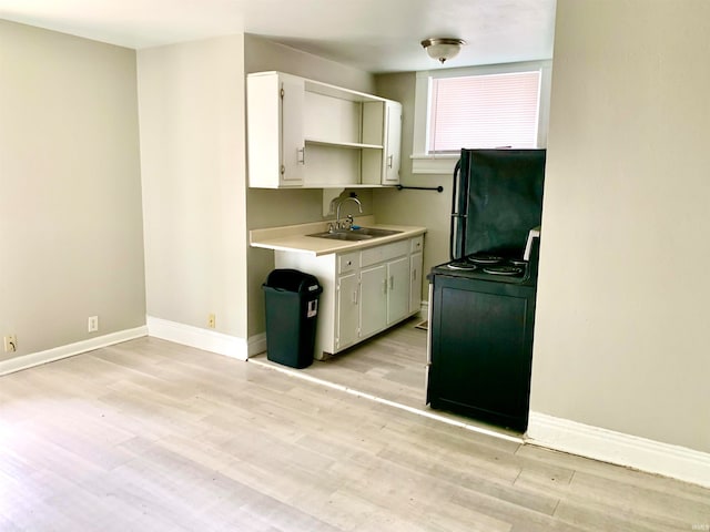 kitchen featuring sink, range, black refrigerator, white cabinets, and light wood-type flooring