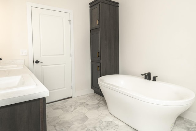 bathroom with baseboards, a freestanding bath, a sink, and double vanity