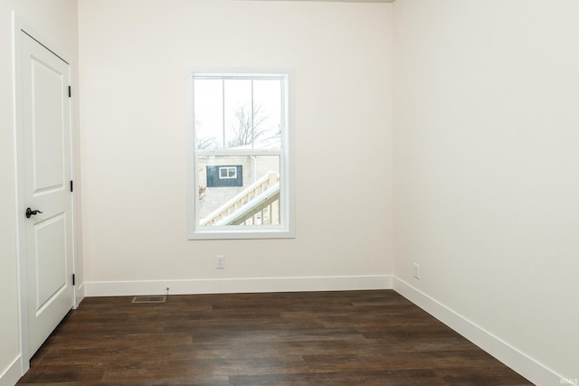 empty room featuring visible vents, baseboards, and dark wood finished floors