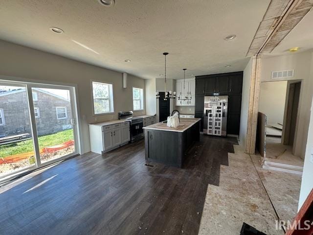 kitchen with hanging light fixtures, dark hardwood / wood-style floors, a center island with sink, and refrigerator