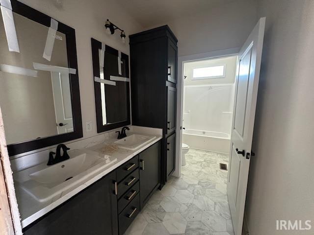 full bath featuring marble finish floor, double vanity, a sink, and toilet