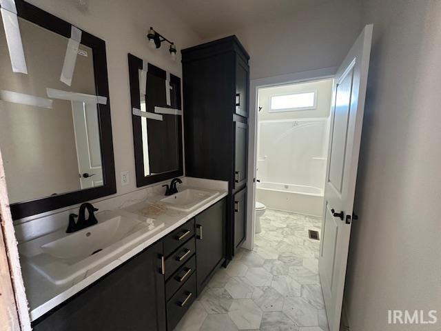 bathroom with marble finish floor, a sink, toilet, and double vanity