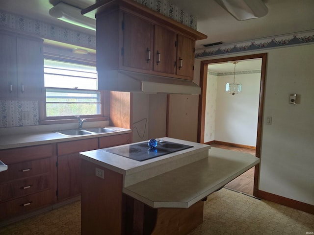 kitchen featuring black electric cooktop, an inviting chandelier, sink, light hardwood / wood-style floors, and decorative light fixtures