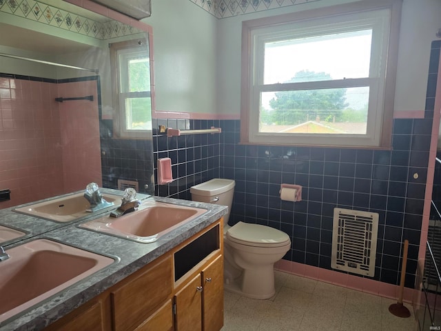 bathroom featuring tile walls, toilet, dual bowl vanity, and a healthy amount of sunlight