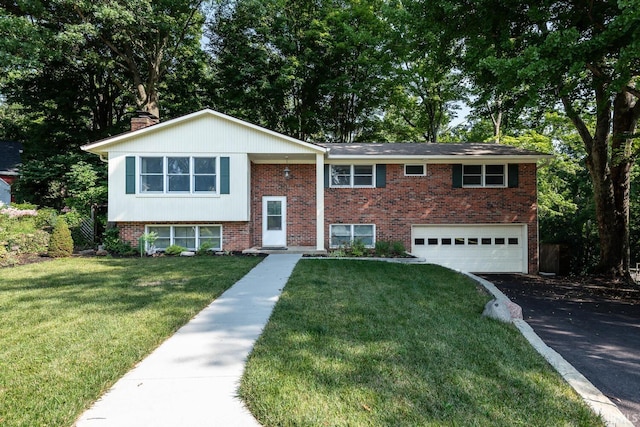 raised ranch with aphalt driveway, an attached garage, brick siding, a chimney, and a front yard