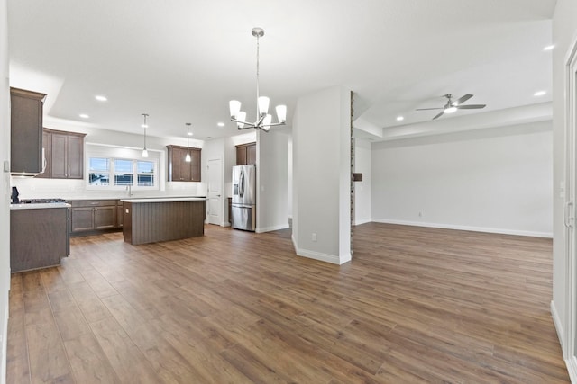 kitchen featuring dark wood-type flooring, stainless steel fridge with ice dispenser, ceiling fan with notable chandelier, a kitchen island, and decorative light fixtures