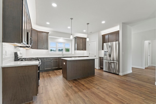 kitchen featuring appliances with stainless steel finishes, a center island, decorative light fixtures, dark hardwood / wood-style floors, and sink