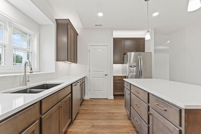 kitchen featuring light wood-type flooring, sink, hanging light fixtures, decorative backsplash, and stainless steel appliances