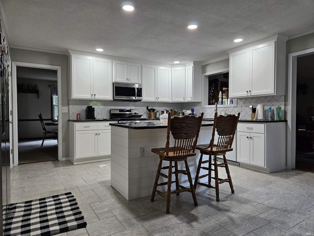 kitchen featuring a breakfast bar area, white cabinets, decorative backsplash, ornamental molding, and stainless steel appliances