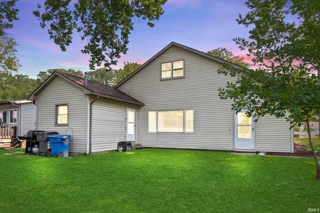 back house at dusk featuring a lawn