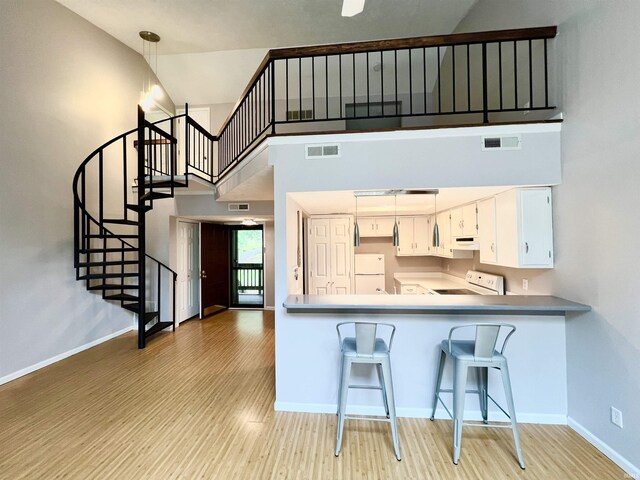 kitchen featuring white appliances, kitchen peninsula, decorative light fixtures, light hardwood / wood-style floors, and white cabinetry