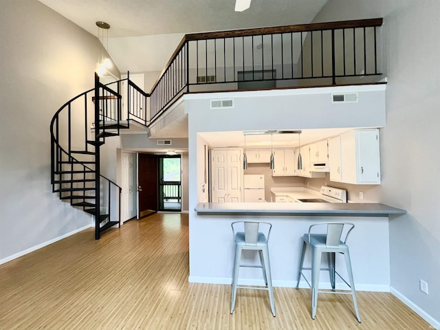 kitchen featuring white cabinetry, stove, a towering ceiling, decorative light fixtures, and kitchen peninsula