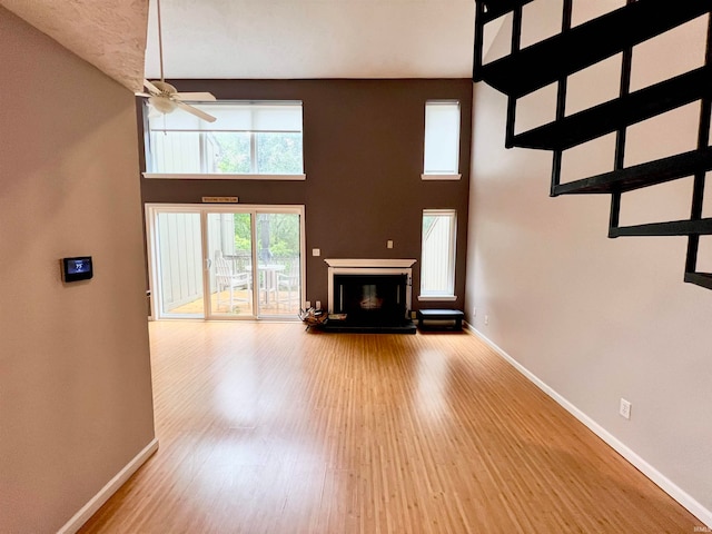 unfurnished living room featuring ceiling fan, a towering ceiling, and light hardwood / wood-style floors