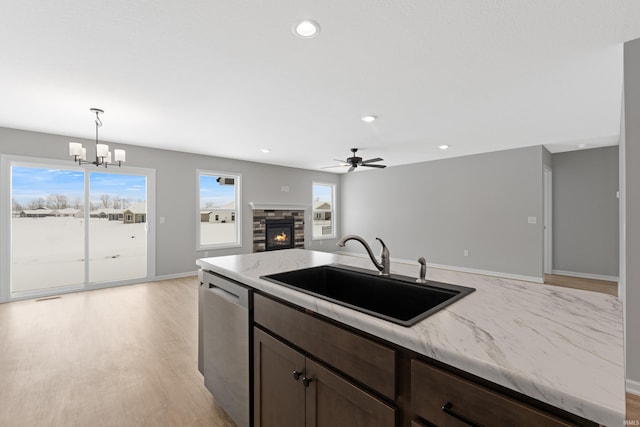 kitchen with dishwasher, a stone fireplace, hanging light fixtures, light stone counters, and sink