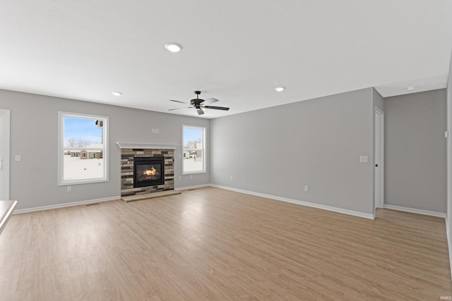 unfurnished living room with light hardwood / wood-style floors, ceiling fan, and a stone fireplace