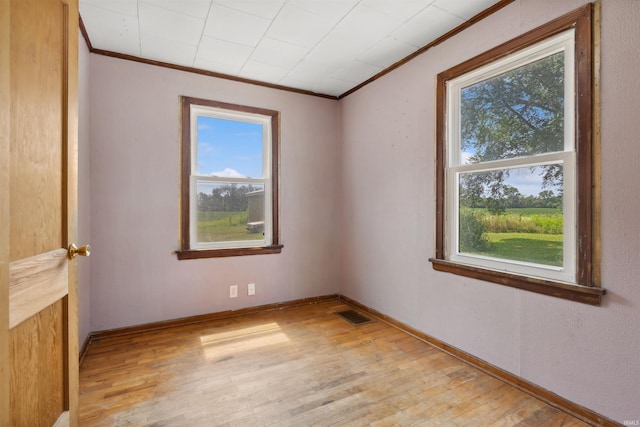 unfurnished room featuring light wood finished floors, visible vents, baseboards, and crown molding