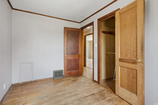 unfurnished bedroom with a closet, visible vents, light wood-style flooring, ornamental molding, and baseboards