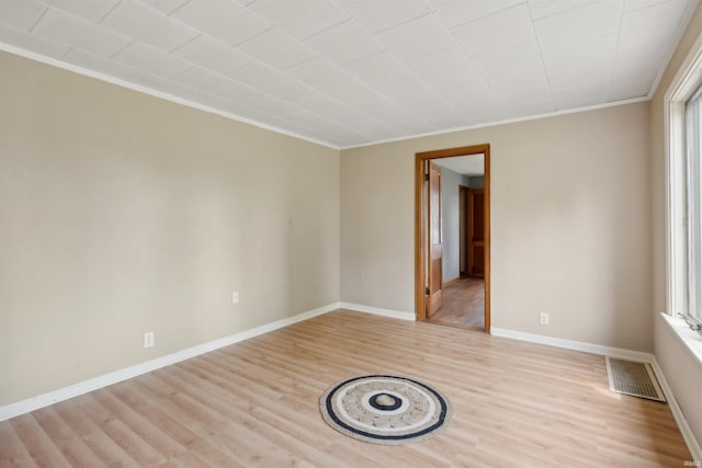 empty room with ornamental molding, light wood-type flooring, visible vents, and baseboards