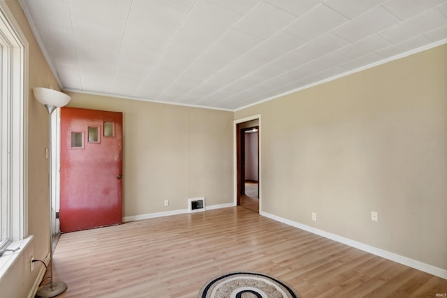 empty room featuring ornamental molding, light wood-type flooring, and baseboards