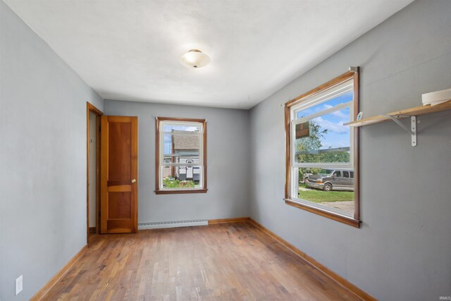 unfurnished room featuring baseboard heating, wood finished floors, and baseboards