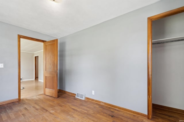 unfurnished bedroom featuring light wood-type flooring, a closet, visible vents, and baseboards