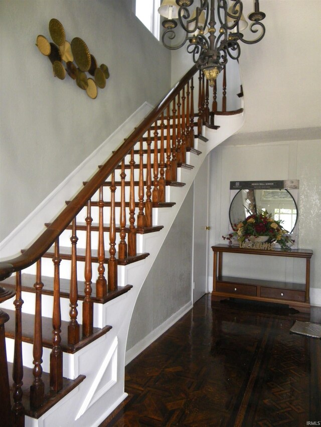 stairway with parquet floors and an inviting chandelier