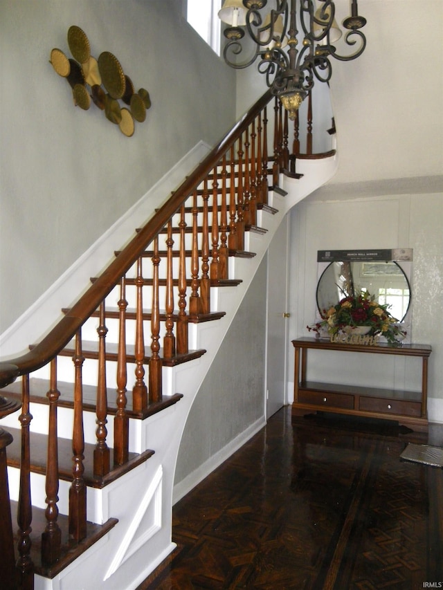 stairway featuring a high ceiling, an inviting chandelier, parquet floors, and a wealth of natural light