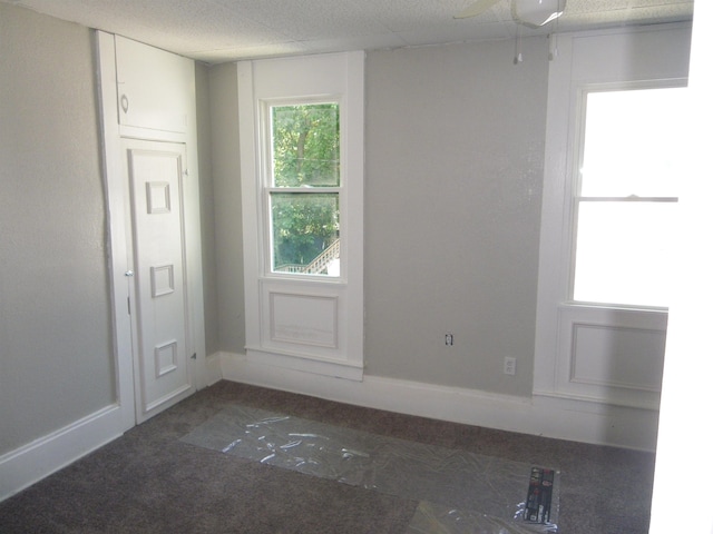 unfurnished room with ceiling fan, a drop ceiling, and dark colored carpet