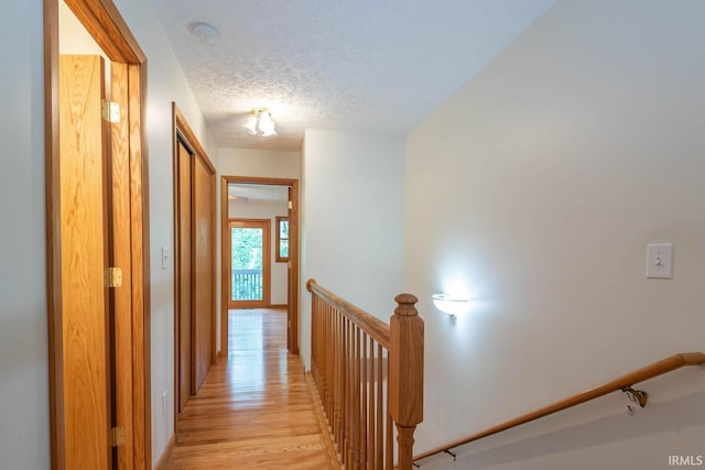 hall with light hardwood / wood-style floors and a textured ceiling