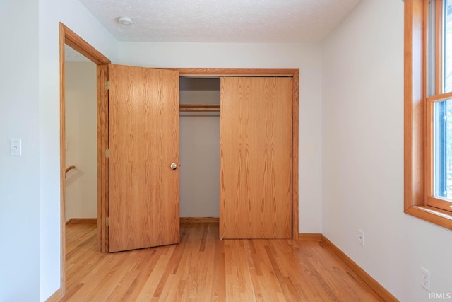 unfurnished bedroom featuring a textured ceiling, a closet, and light wood-type flooring