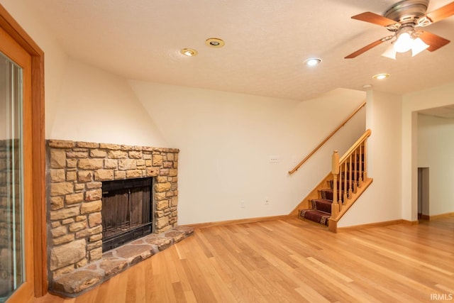 unfurnished living room with a stone fireplace, light hardwood / wood-style floors, and ceiling fan