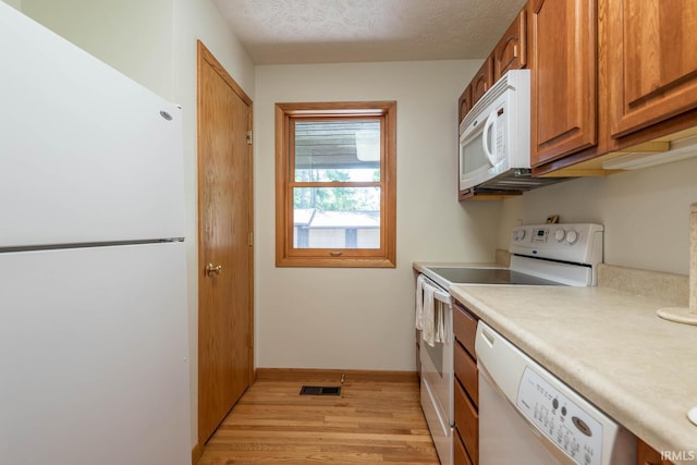 kitchen featuring light wood-type flooring, a textured ceiling, and white appliances