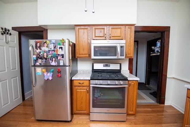 kitchen with light hardwood / wood-style flooring, appliances with stainless steel finishes, and light stone counters